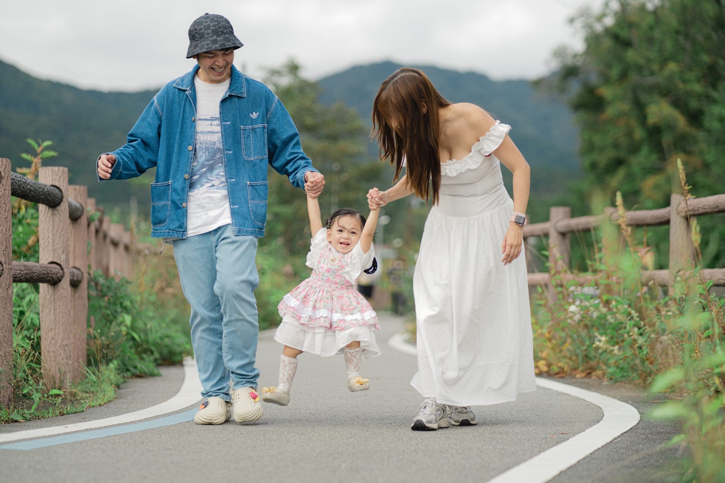 Parents swinging their toddler by the hands as they walk a lakeside path