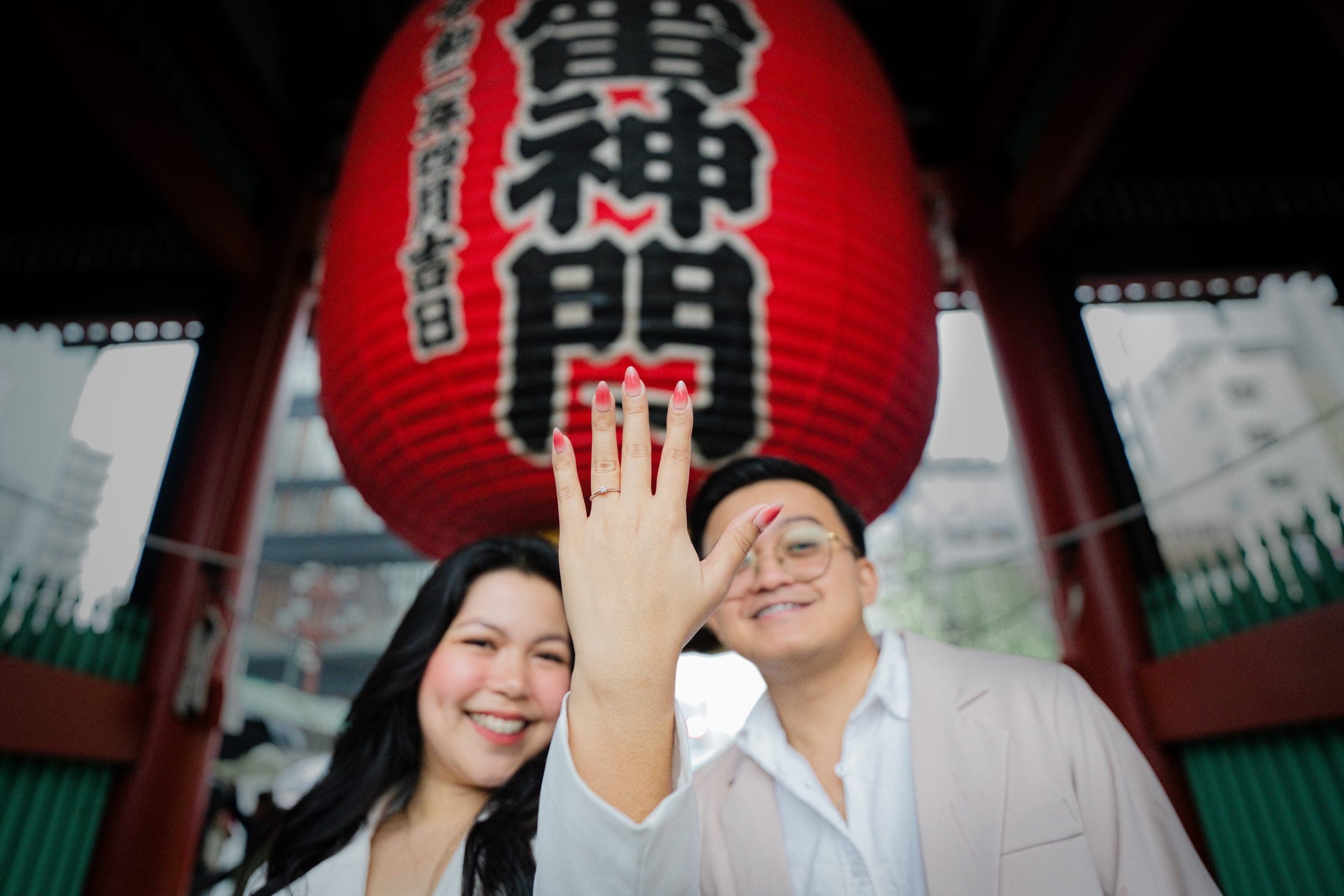 A newly engaged couple beneath the great red lantern at Kaminarimon, her ring hand raised